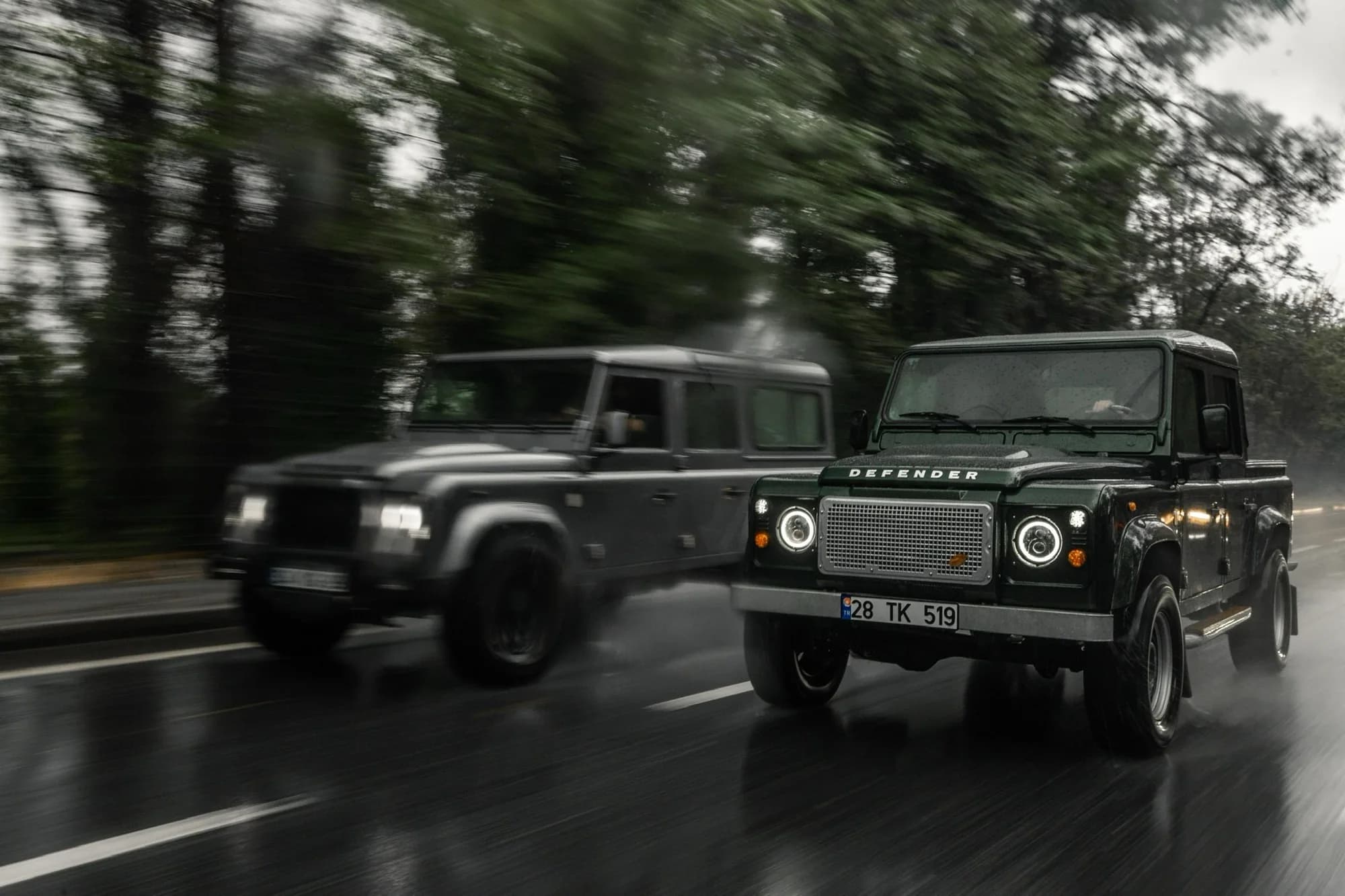 Two Defenders driving together on a wet forest road