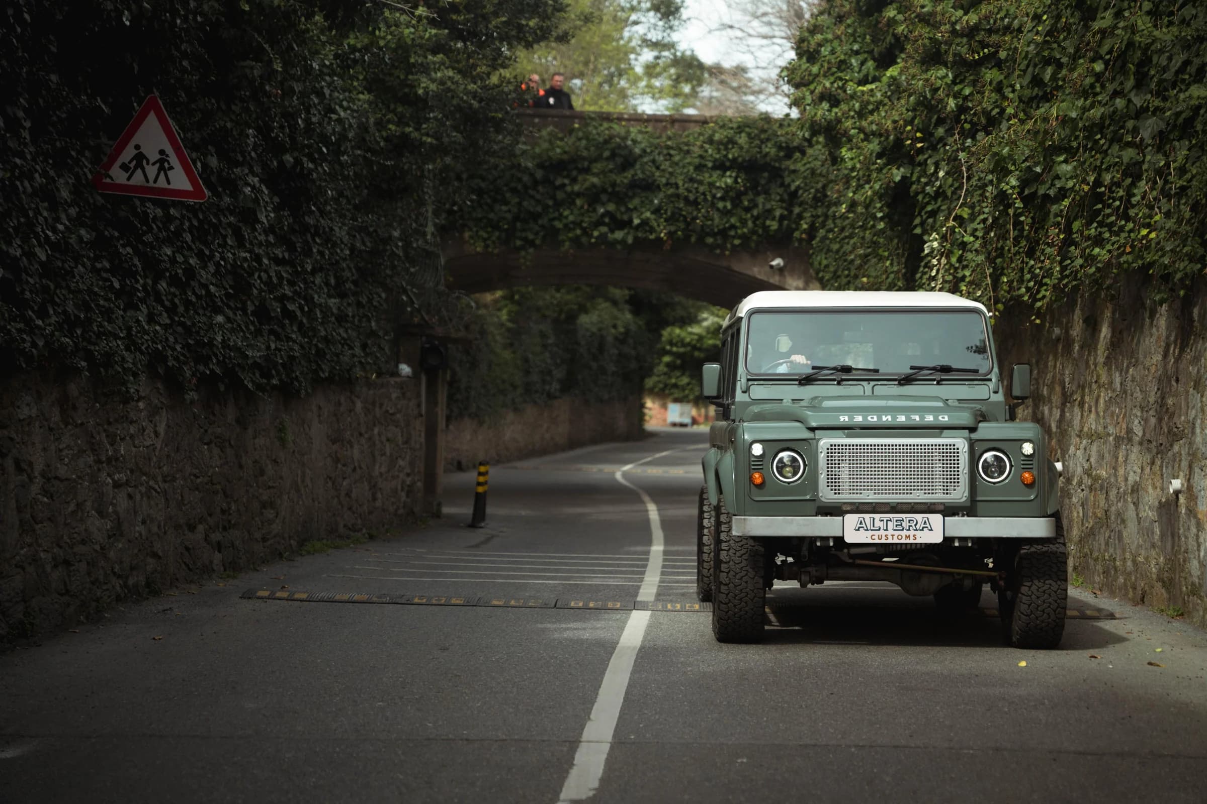 Green Altera Defender on a narrow tree-lined road